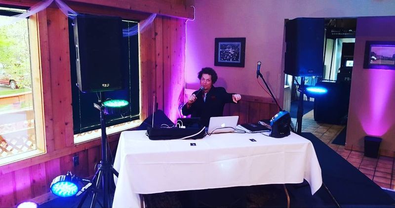 Dave Menzo on the microphone at his DJ booth under purple uplighting at Brookshire Inn