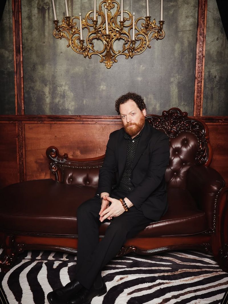 Dave Menzo seated on a leather sofa beneath a chandelier