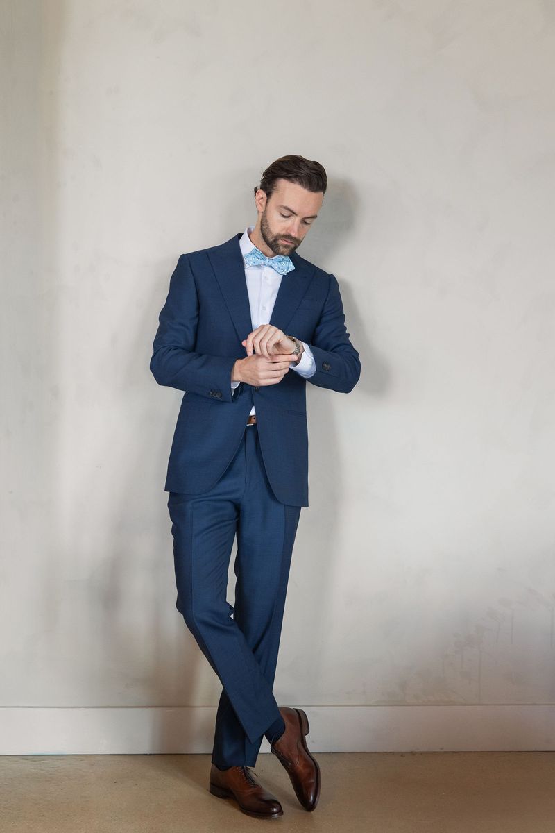 Dennis leaning on a wall in his navy suit