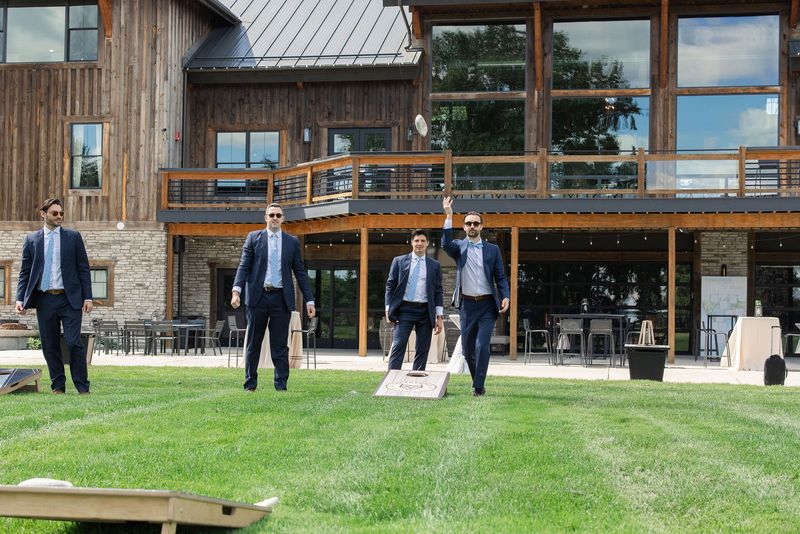 Groomsmen playing cornhole on the lawn outside Revel Run's timber hall