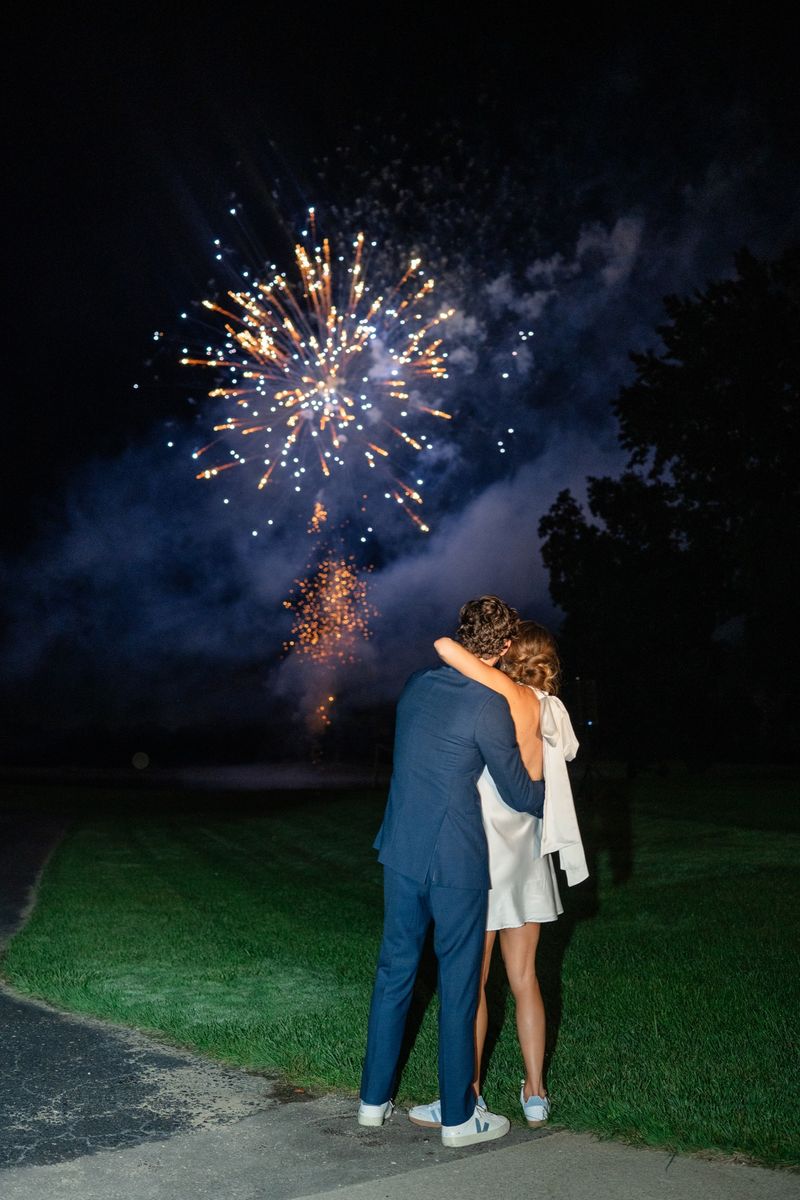 Katie and Dennis holding each other as fireworks burst over the trees