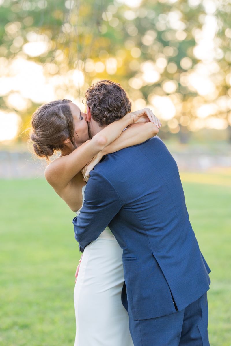 Katie and Dennis kissing on the lawn in golden evening light