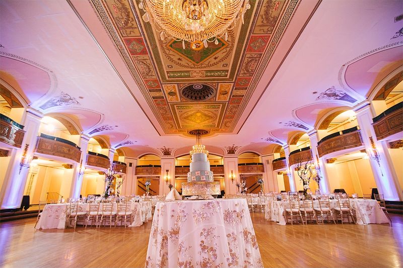 The ballroom at The Masonic Temple set for dinner under chandeliers and pink light